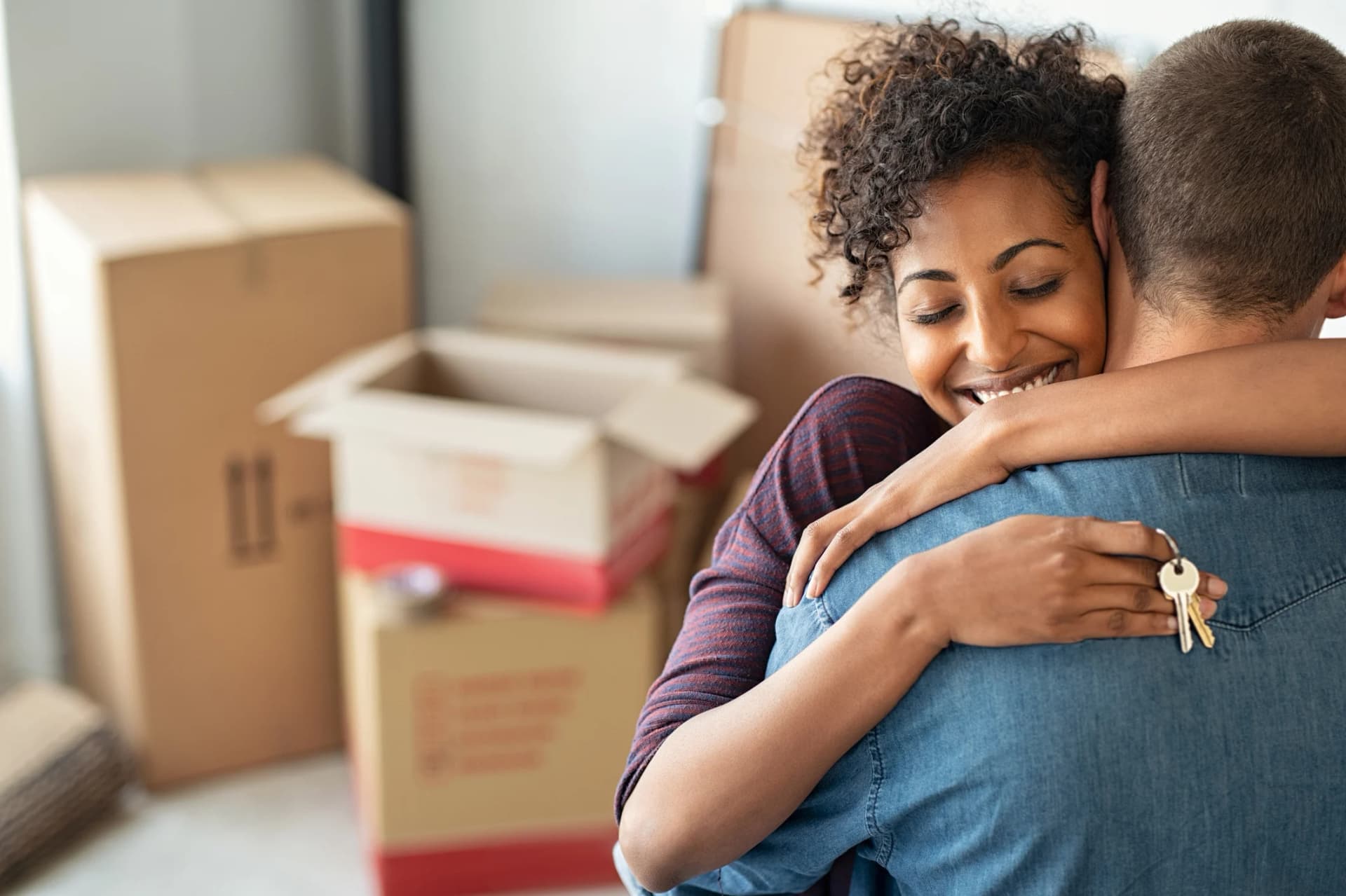 couple qui se serre dans les bras en souriant devant un tas de cartons heureux de déménager sereinement